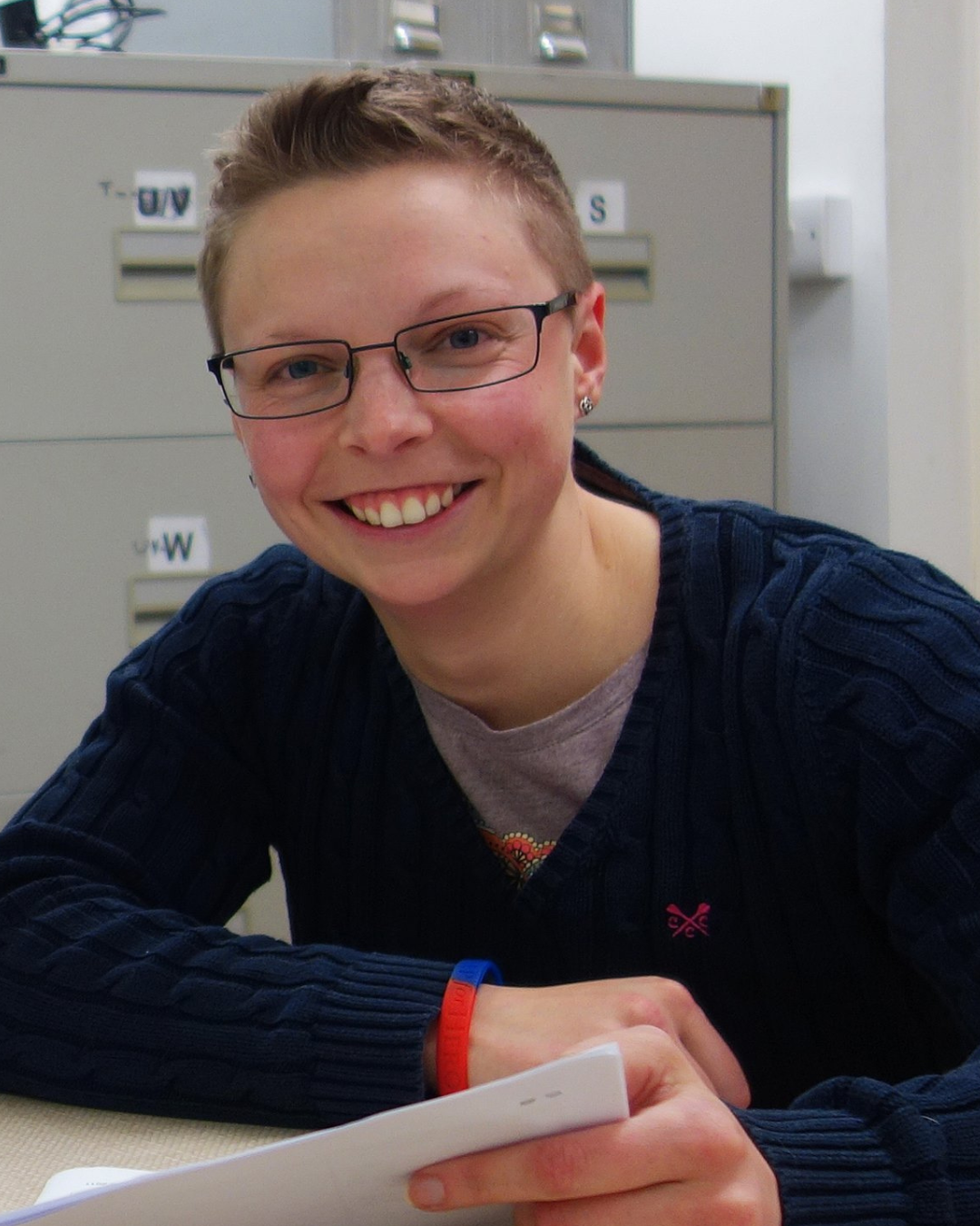 Photo of Jade smiling to camera - a white woman with short cropped hair and glasses